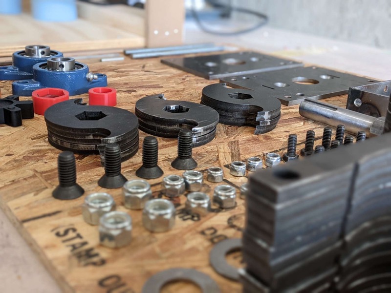 Parts for an earlier shredder build laid out before assembly: cut blades and spacers with hex bores, flange bearings, side plates, and fasteners.